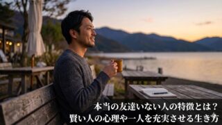 夕暮れの湖畔で一人、穏やかな表情で佇む日本人男性。画像下部には記事タイトル「友達いない人の特徴とは？賢い人の心理や一人を充実させる生き方」のテキストが入っている。